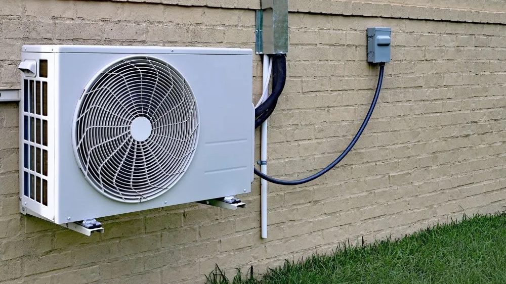White mini split outdoor condenser mounted on a tan brick wall with line set cover, a mini split for garage 2026 installation